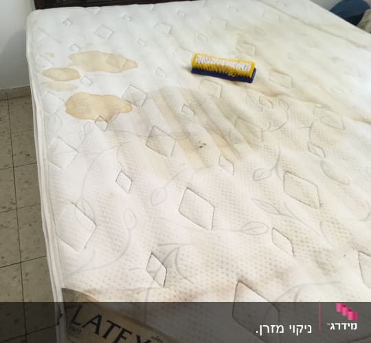 מזרן עם כתמים ומברשת ניקוי מונחת עליו